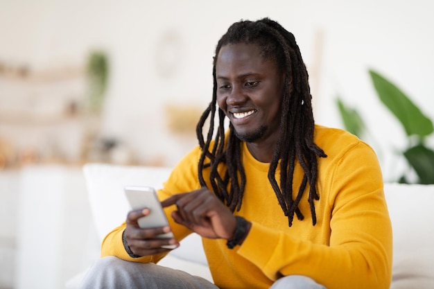 Hombre de ocio digital navegando por las redes sociales en el teléfono inteligente mientras se relaja en casa