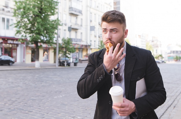 El hombre ocupado con una taza de café y un sándwich en sus manos tiene prisa por trabajar.