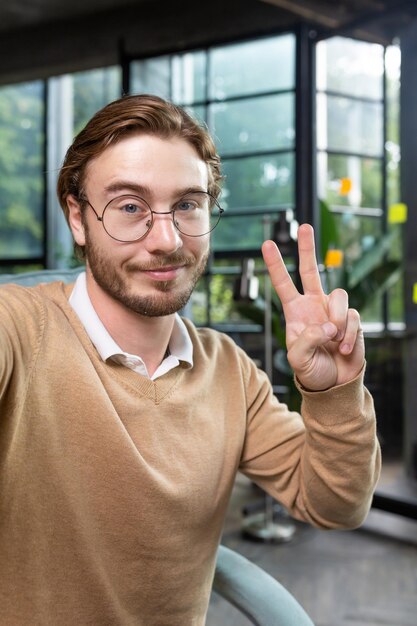 Hombre en la oficina con camisa y gafas sonriendo y mirando la cámara del teléfono inteligente.