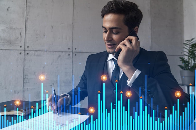 Un hombre en la oficina firmando papeles mientras habla por teléfono y gráfico del mercado de valores y holograma de gráfico Doble exposición Ropa formal