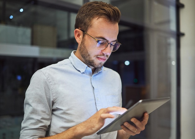 Hombre en la oficina por la noche con tableta digital y trabajando horas extras Hombre de negocios profesional en una empresa de marketing en línea que planifica una estrategia corporativa y prueba una nueva función web para aumentar el crecimiento