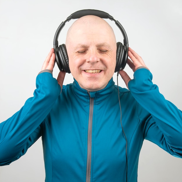 Hombre con los ojos cerrados escucha música con auriculares sobre un fondo claro