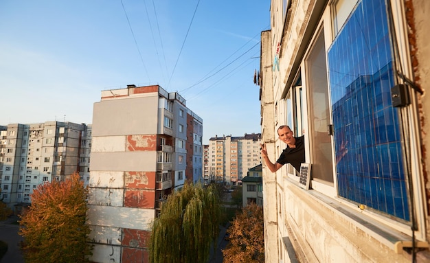 El hombre ondea en el balcón de un edificio de varios pisos equipado con panel solar, fondo urbano