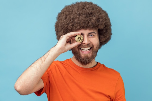 Hombre optimista que cubre el ojo con bitcoin de oro que tiene moneda criptográfica de expresión positiva