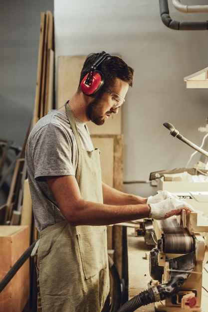 Hombre en orejeras trabajando en lijadora de banda