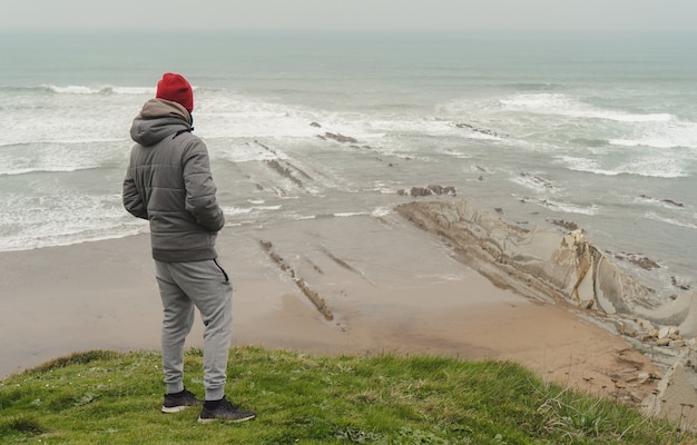 Hombre en la orilla nublada mirando el mar sobre la hierba