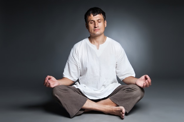 Hombre pacífico haciendo yoga y meditando sobre fondo oscuro