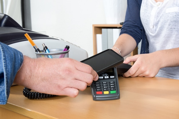 Hombre pagando con tecnología NFC en tarjeta de crédito con teléfono, en restaurante, tienda,