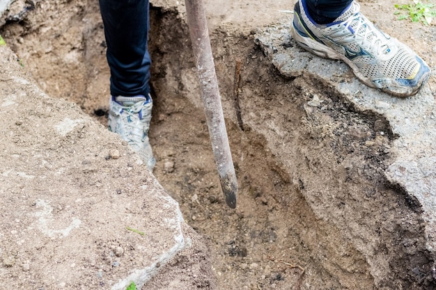 Hombre con una palanca aplasta el suelo duro mientras cava una zanja en un sitio de construcción