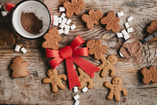 Hombre de pan de jengibre cacao y galletas con un gran lazo rojo sobre un fondo de madera vista superior Varios dulces navideños con una taza de cacao sobre la mesa