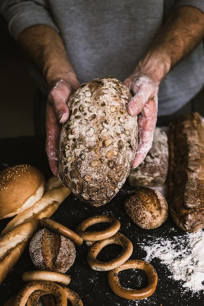 Hombre panadero sosteniendo una hogaza de pan orgánico rústico en sus manos