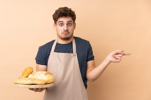 Hombre panadero sosteniendo una mesa con varios panes en beige apuntando a los laterales que tienen dudas