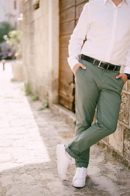 Hombre de pantalón verde y blanca está contra la pared de una casa de piedra closeup | Foto Premium