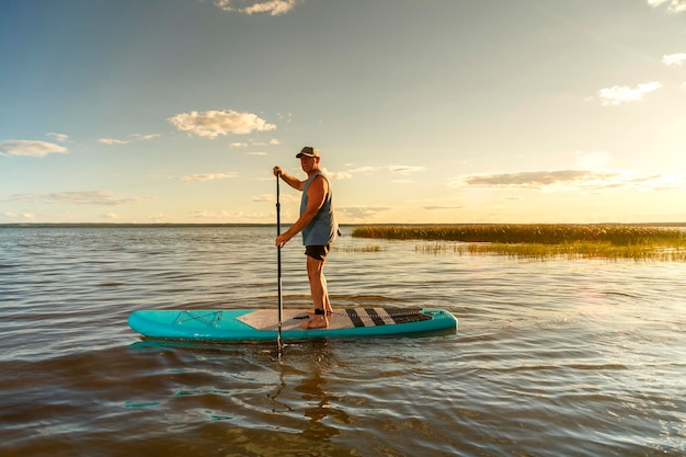 Foto un hombre en pantalones cortos con un remo en una tabla de sup al atardecer en el lago