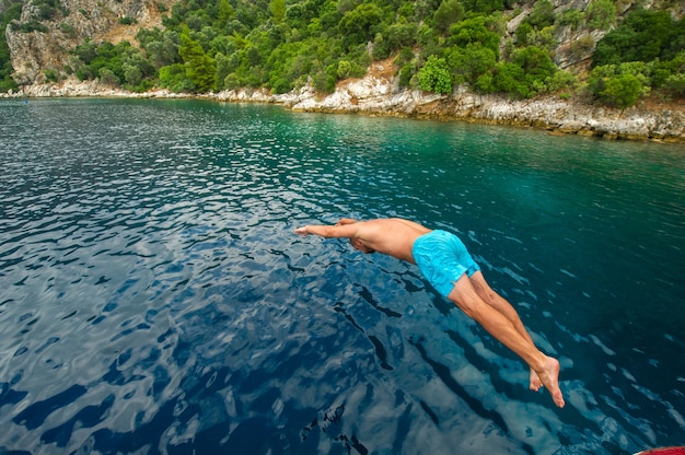 Un hombre con pantalones cortos se zambulle desde un barco en el mar cerca de la orilla.