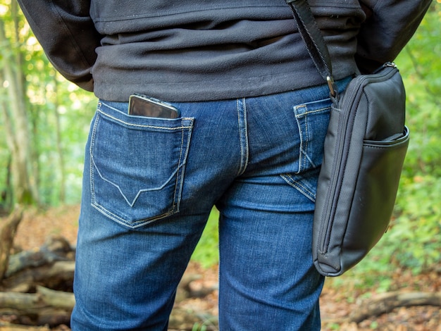 Un hombre con pantalones vaqueros y con una bolsa en el hombro está de pie con la espalda.