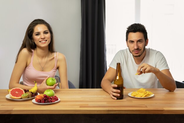 Hombre con papas fritas y cerveza y mujer con frutas