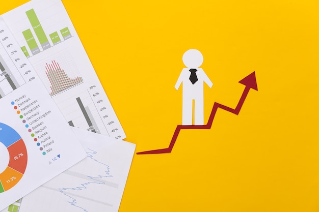 Hombre de papel con flecha de crecimiento, gráficos y tablas. Símbolo de éxito económico y social, escalera al progreso.