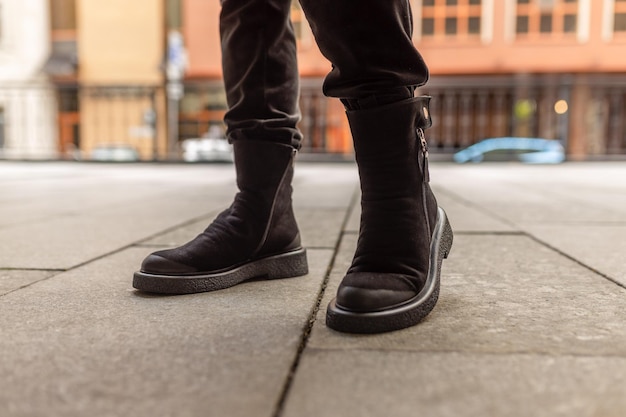 Un hombre con un par de botas de gamuza negra se para en una acera.