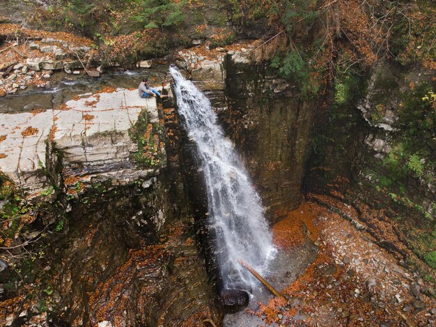 Hombre parado en el acantilado mirando el tiempo de otoño de la cascada