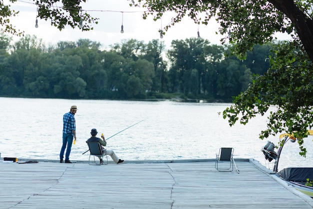 Hombre parado cerca de un anciano sentado y pescando