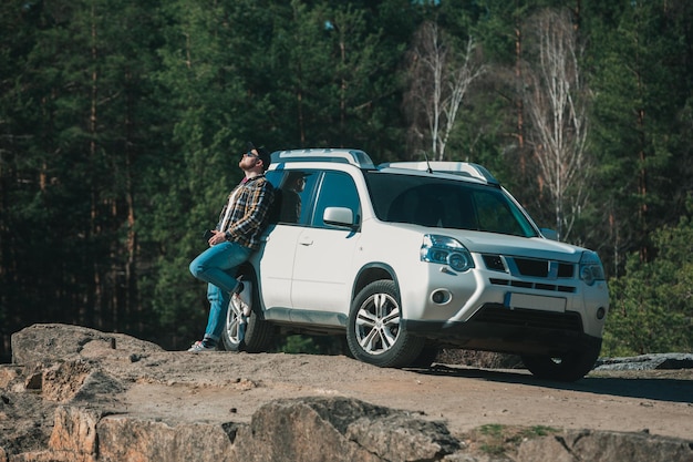 El hombre parado cerca de un automóvil suv blanco disfruta del momento en el concepto de libertad de viaje en automóvil