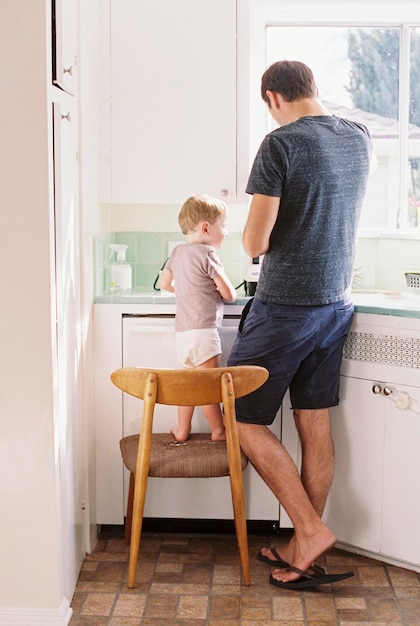 Hombre parado en una cocina con su hijo parado en una silla a su lado