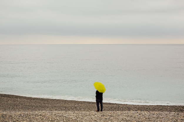 Hombre con un paraguas amarillo en la orilla del mar Mediterráneo