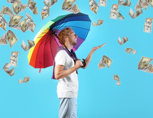 Hombre con paraguas de arco iris bajo lluvia de dinero sobre fondo de color