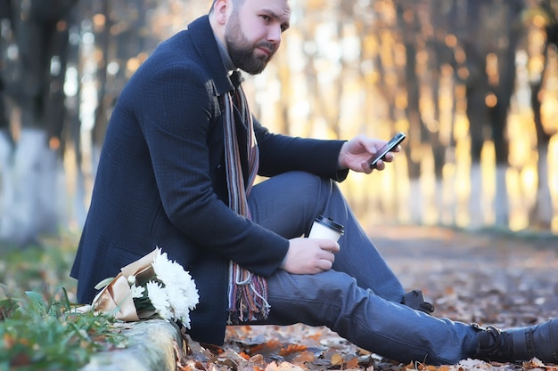 Hombre en el parque de otoño al aire libre con ramo de flores esperando fecha