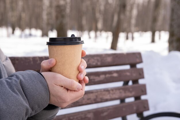 Hombre en el parque sosteniendo una taza de papel con café en el fondo de un banco