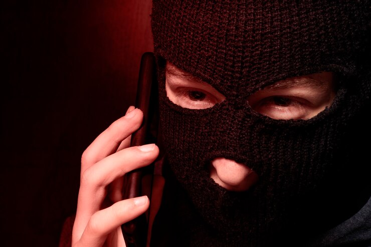 Foto un hombre con un pasamontañas está hablando por un teléfono móvil. el concepto de fraude en internet, piratería de sistemas de pago, piratería de billeteras electrónicas.