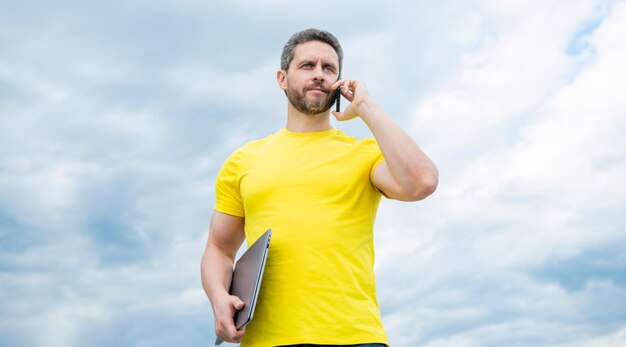 Hombre con pc hablando por teléfono inteligente en el fondo del cielo