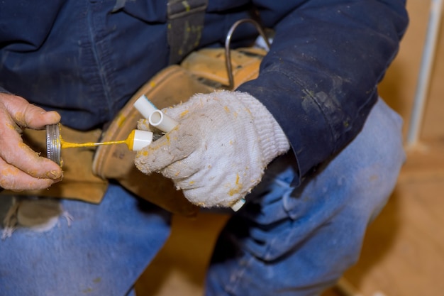 Hombre pegando piezas de pegamento de cemento de un trozo de tubos de polipropileno para la instalación de la línea de agua de una nueva casa en construcción