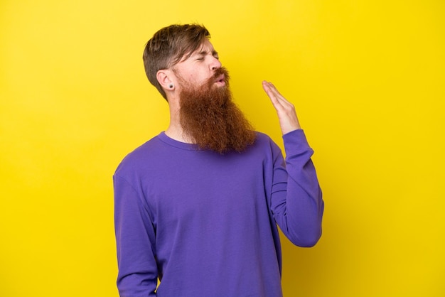 Hombre pelirrojo con barba aislado de fondo amarillo con expresión cansada y enferma