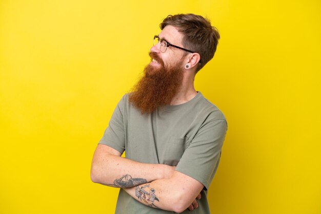 Hombre pelirrojo con barba aislado de fondo amarillo mirando hacia un lado y sonriendo