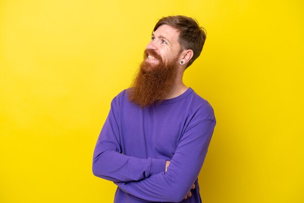 Hombre pelirrojo con barba aislado de fondo amarillo mirando hacia un lado y sonriendo