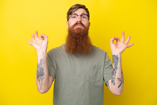 Hombre pelirrojo con barba aislado sobre fondo amarillo en pose zen