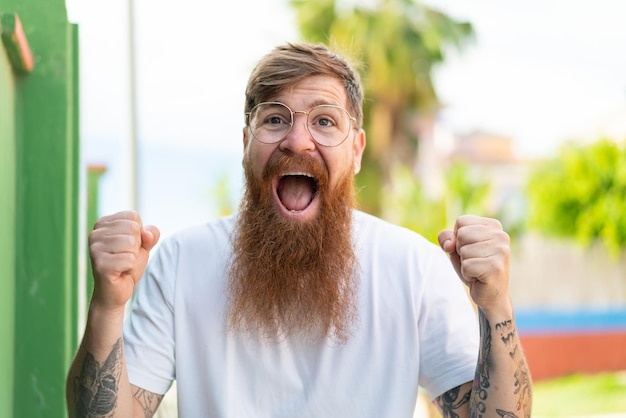 Hombre pelirrojo con barba con gafas y celebrando una victoria