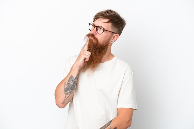 Hombre pelirrojo con barba larga aislado de fondo blanco que tiene dudas mientras mira hacia arriba