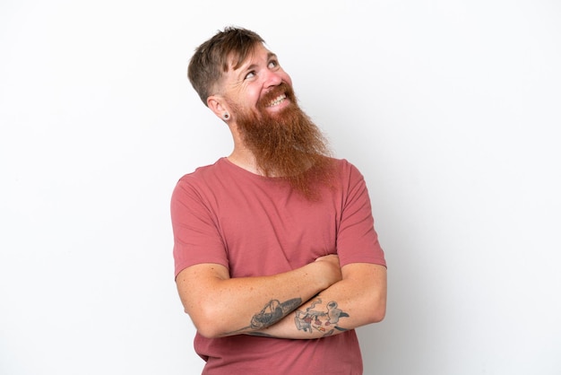 Hombre pelirrojo con barba larga aislado sobre fondo blanco mirando hacia arriba mientras sonríe