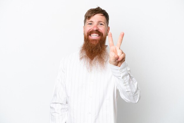 Hombre pelirrojo con barba larga aislado sobre fondo blanco sonriendo y mostrando el signo de la victoria