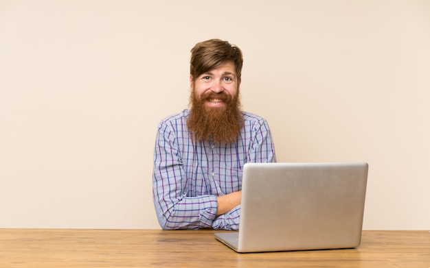 Hombre pelirrojo con barba larga en una mesa con un portátil riendo