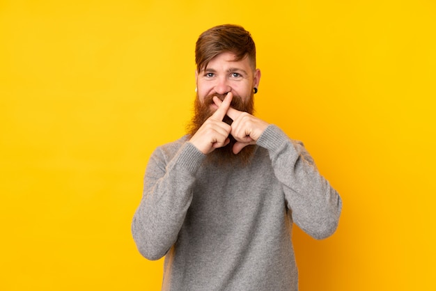 Hombre pelirrojo con barba larga sobre amarillo aislado mostrando un signo de gesto de silencio