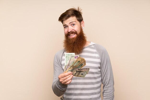 Hombre pelirrojo con barba larga sobre fondo aislado tomando mucho dinero