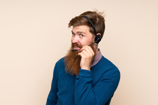 Hombre pelirrojo con barba larga sobre fondo aislado trabajando con auriculares mirando lateral