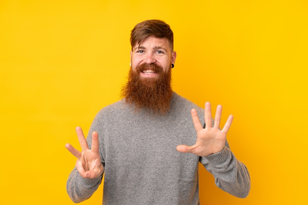 Hombre pelirrojo con barba larga sobre pared amarilla aislada contando ocho con los dedos