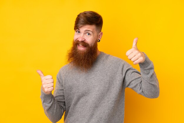 Hombre pelirrojo con barba larga sobre pared amarilla con pulgares arriba gesto y sonriendo