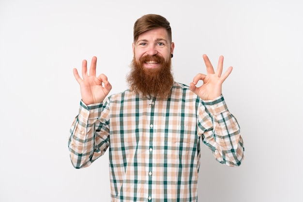 Hombre pelirrojo con barba larga sobre pared blanca que muestra un signo bien con los dedos