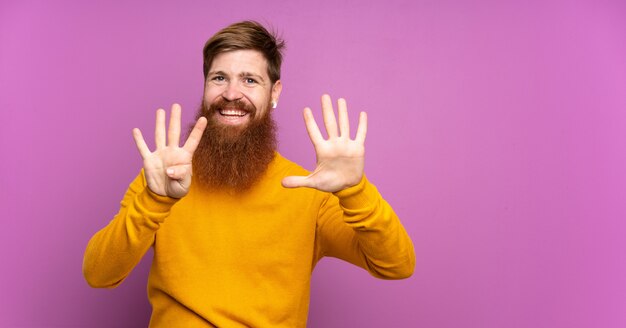 Hombre pelirrojo con barba larga sobre púrpura aislado contando nueve con los dedos